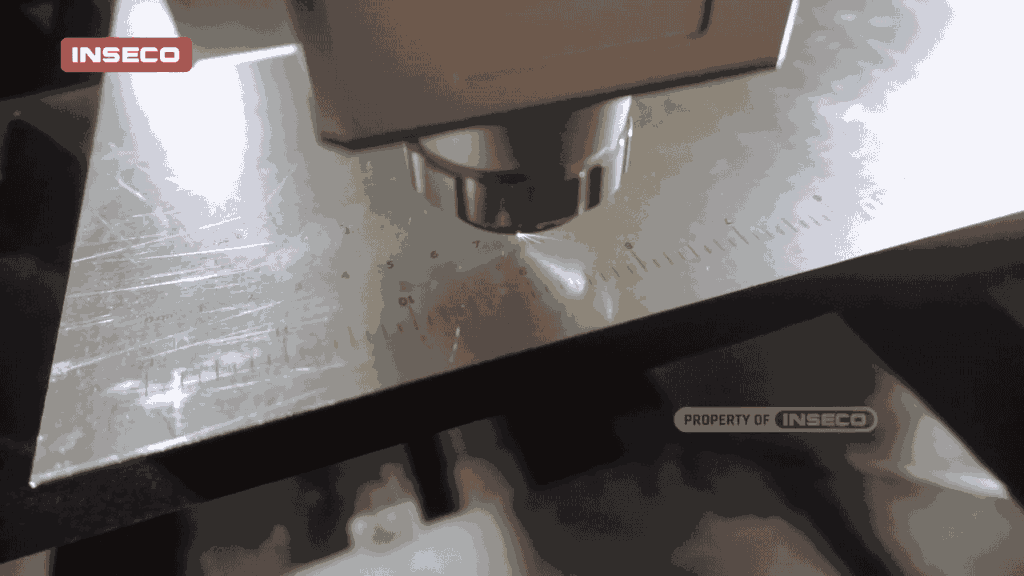 Detail close-up mesin fiber laser CNC dengan fokus pada pemotongan plat besi menggunakan alat pemotong yang presisi, dengan penanda pengukur untuk akurasi tinggi.