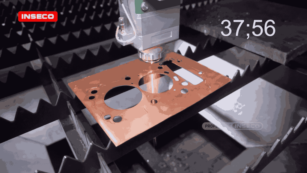 Kepala laser sedang membentuk lubang presisi pada lembaran tembaga, potongan bulat dan persegi terlihat rapi di permukaan material.