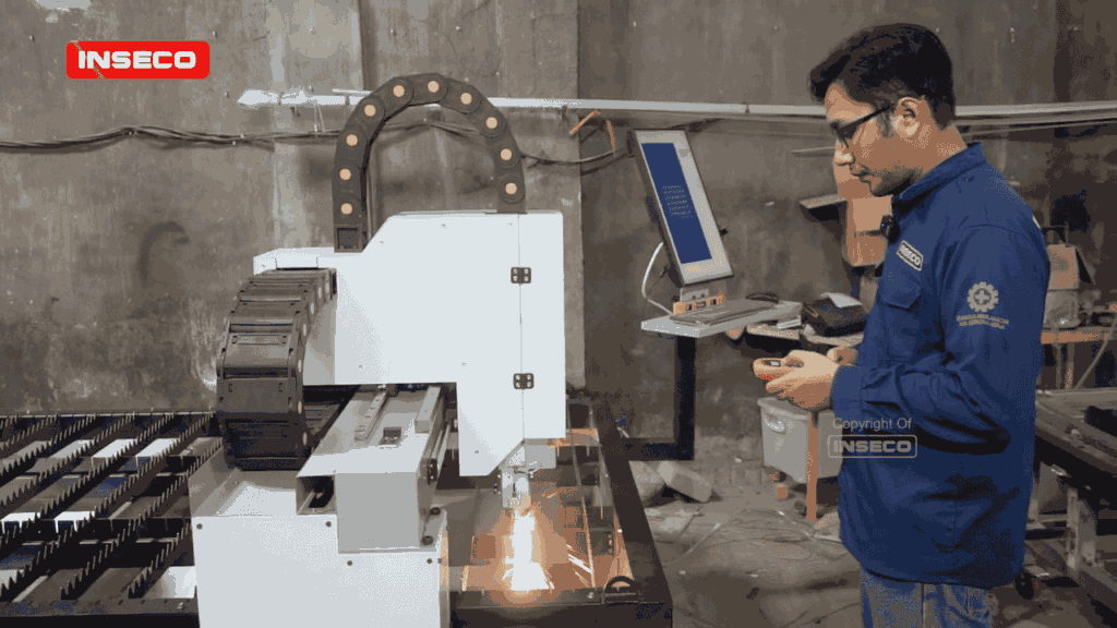 Mesin pemotong laser CNC yang sedang beraksi, memotong pola rumit pada lembaran logam. Kepala laser terfokus pada material, menciptakan potongan tajam dan bersih