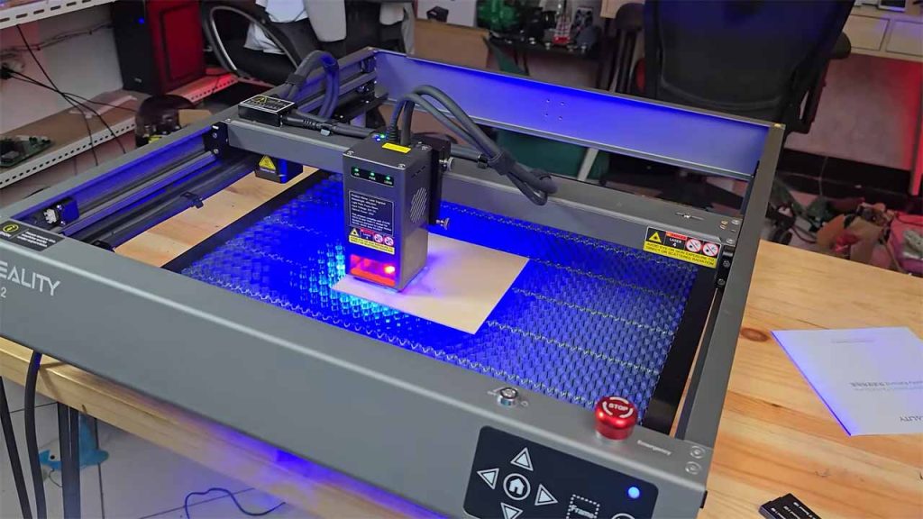 Mesin laser cutting sedang memotong pola rumit pada selembar kayu lapis, menunjukkan sinar laser yang terang dan presisi